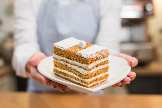 Foto gratuita primer plano de un panadero femenino que sirve la rebanada de los pasteles en la placa blanca de la forma del corazón