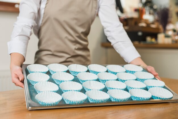 Primer plano de panadero femenino que sostiene la bandeja de acero inoxidable con moldes de silicona de cupcake dispuestos