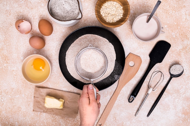 Primer plano de panadero tamizando harina para la masa con ingredientes sobre fondo texturizado