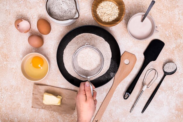 Primer plano de panadero tamizando harina para la masa con ingredientes sobre fondo texturizado