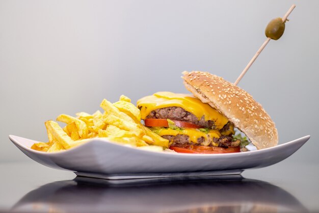 Primer plano de papas fritas y una hamburguesa en un plato bajo las luces contra una pared blanca