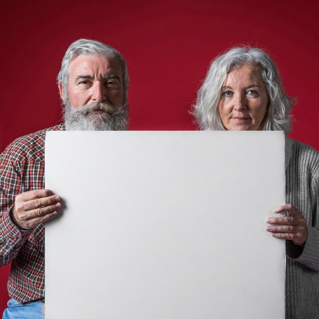 Primer plano de un par mayor que sostiene el cartel blanco en blanco contra el contexto coloreado