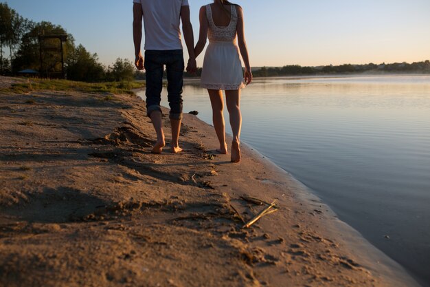 Primer plano de pareja cogidos de la mano con la playa de fondo