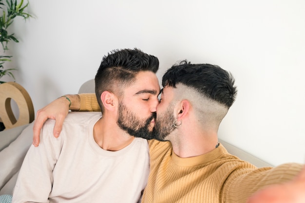 Primer plano de la pareja gay joven romántica besándose tomando selfie