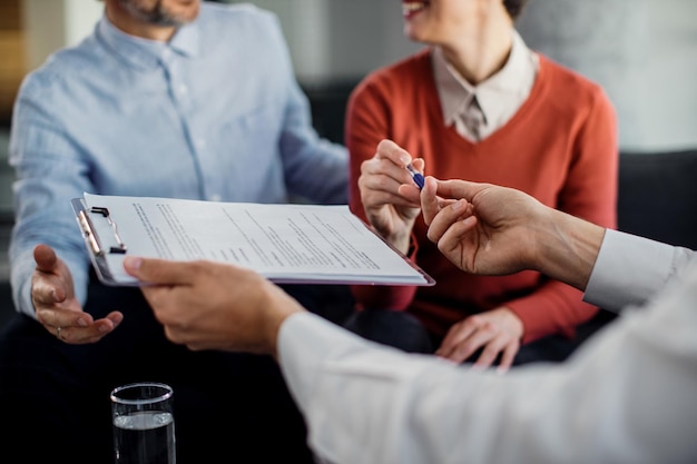 Primer plano de una pareja irreconocible que firma un contrato con un asesor financiero