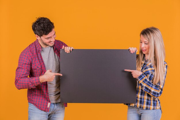 Primer plano de una pareja joven que señala sus dedos en el cartel negro sobre un fondo naranja