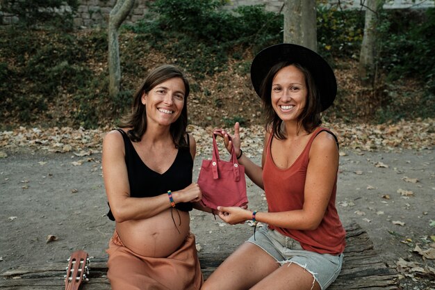 Primer plano de una pareja de lesbianas embarazadas intercambiando una pequeña bolsa rosa