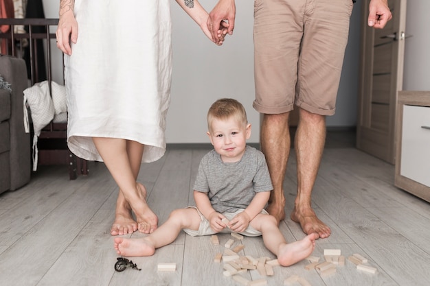 Primer plano de una pareja de pie detrás del niño jugando con bloques de madera