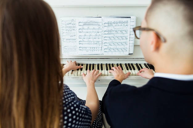 Primer plano de pareja tocando el piano con la hoja musical