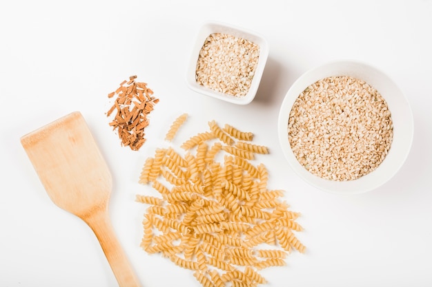 Primer plano de pasta fusilli sin cocer; Arroz y canela molida con espátula sobre fondo blanco