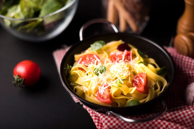 Primer plano de pasta tagliatelle saludable con queso en un recipiente con rodajas de tomate cherry