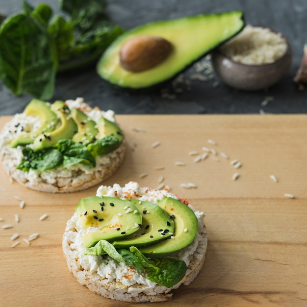 Primer plano de pastel de arroz con rebanadas de aguacate; sobre tabla de cortar de madera