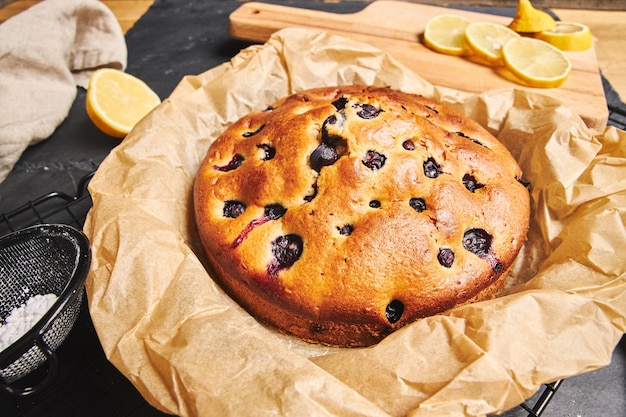 Primer plano de un pastel de cerezas con azúcar en polvo e ingredientes en el lado negro