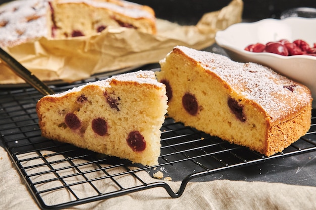 Primer plano de un pastel de cerezas con azúcar en polvo e ingredientes en el lado negro