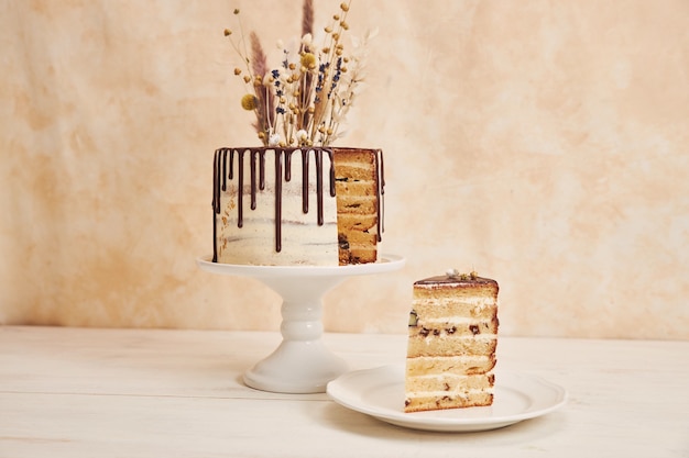 Primer plano de un pastel de vainilla con goteo de chocolate y flores en la parte superior