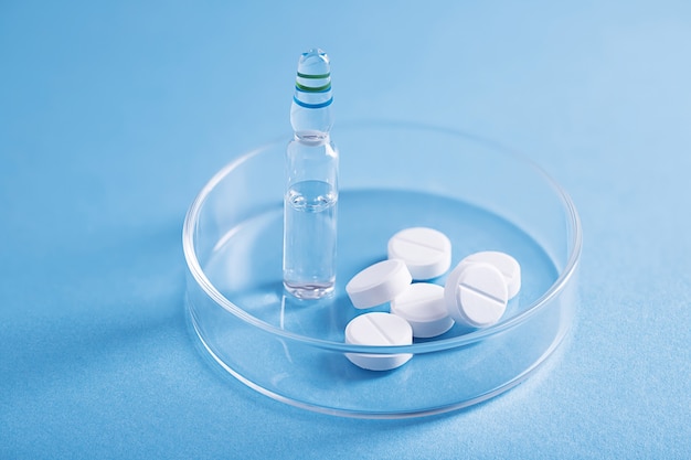 Primer plano de pastillas blancas y un frasco de líquido transparente en un plato de vidrio en un laboratorio