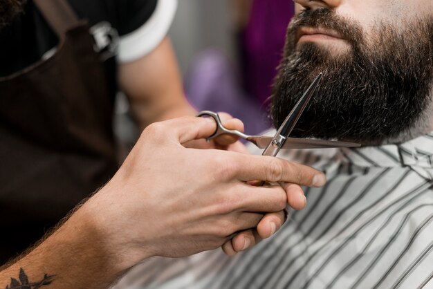 Primer plano, de, un, peluquero, mano corte, barba del hombre, con, tijeras