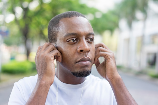 Primer plano de pensativo turista negro escuchando música y caminando al aire libre.