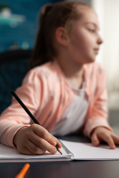 Primer plano de una pequeña colegiala que estudia la lección en línea trabajando en la tarea de matemáticas