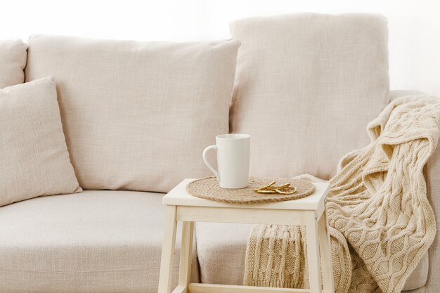 Primer plano de una pequeña mesa con una taza cerca de un sofá beige bajo las luces