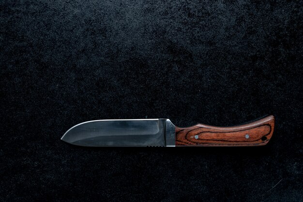 Primer plano de un pequeño cuchillo afilado con mango marrón sobre un fondo negro