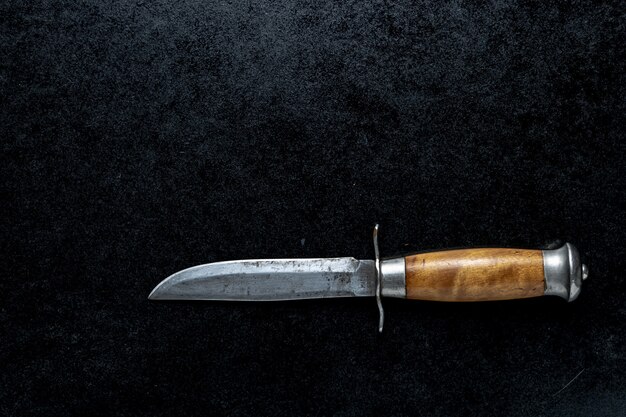 Primer plano de un pequeño cuchillo afilado con mango marrón sobre un fondo negro
