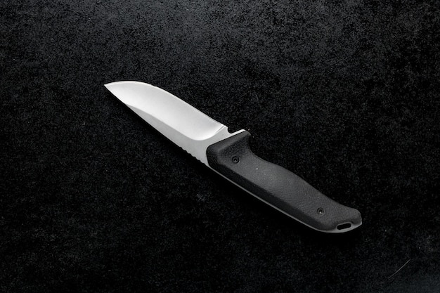Primer plano de un pequeño cuchillo de combate con mango negro sobre la mesa