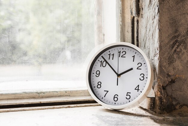 Primer plano de un pequeño reloj redondo blanco cerca de la ventana de cristal