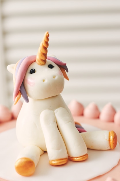 Primer plano de un pequeño unicornio en la parte superior de un pastel de cumpleaños bajo las luces con un fondo borroso