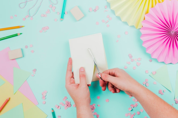 Primer plano de una persona cortando el papel con tijera sobre fondo verde azulado