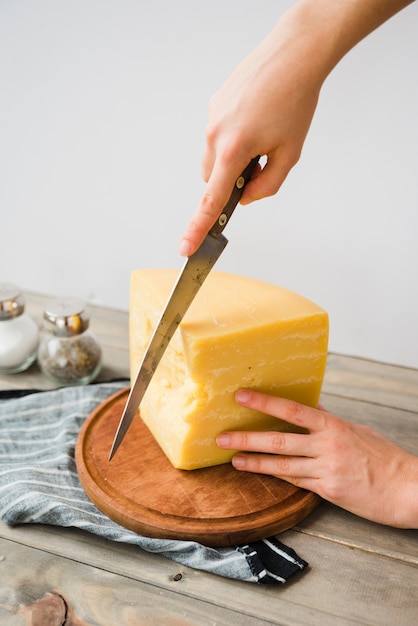 Foto gratuita primer plano de una persona cortando el queso con un cuchillo en una tabla de cortar redonda