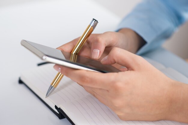 Primer plano de una persona enviando mensajes de texto en un teléfono inteligente y trabajando en el escritorio