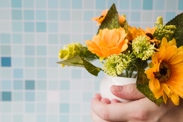 Primer plano de una persona con florero en la mano contra los azulejos de mosaico