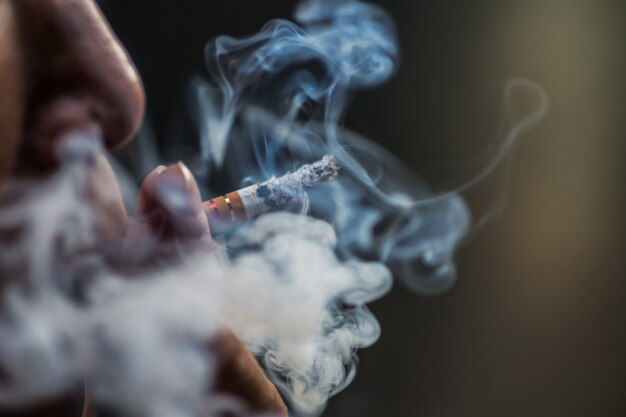 Primer plano de una persona fumando un cigarrillo rodeado de humo
