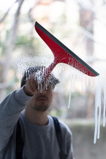 Primer plano de una persona limpiando ventanas con una escobilla de goma roja