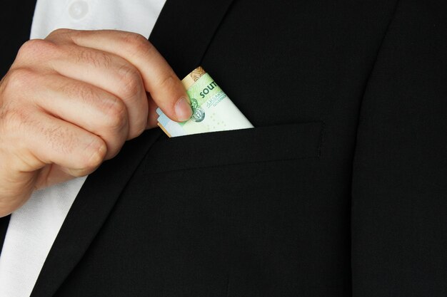 Primer plano de una persona poniendo algo de dinero en efectivo en el bolsillo de su abrigo