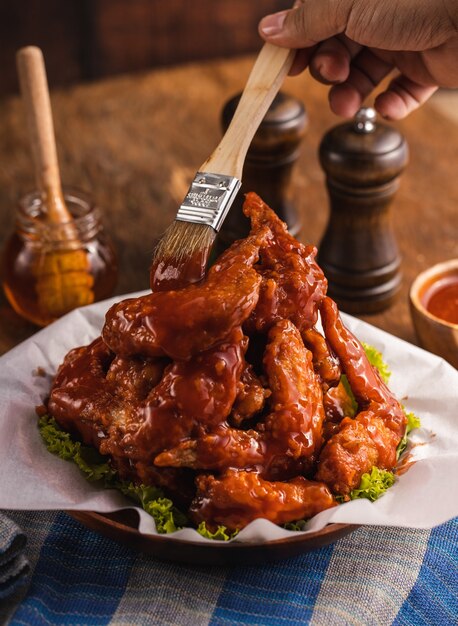 Primer plano de una persona poniendo salsa en alitas de pollo deliciosamente cocidas en un recipiente sobre la mesa