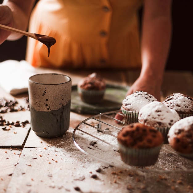 Primer plano de una persona preparando chocolate derretido en vaso con cupcakes