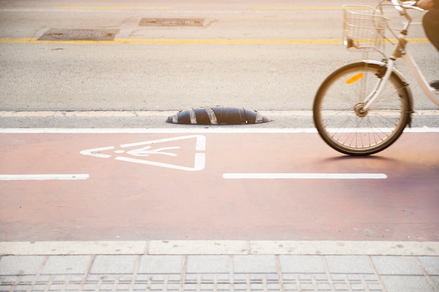 Foto gratuita primer plano de una persona que monta la bicicleta en una carretera con un signo de advertencia de triángulo