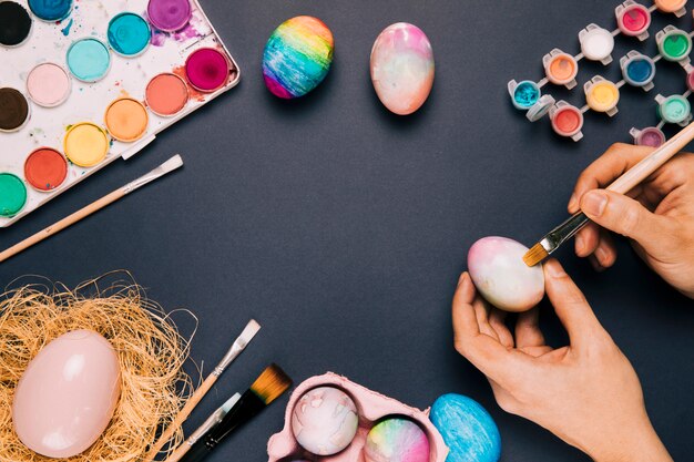 Primer plano de una persona que pinta el huevo de Pascua con pincel sobre fondo negro