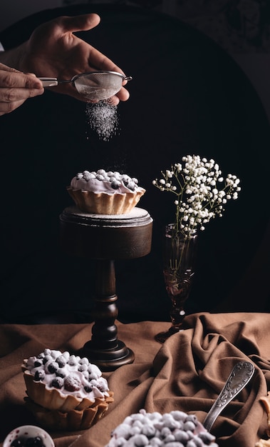 Primer plano de una persona que quita el polvo de azúcar en una tarta de frutas con el florero de flores