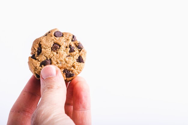 Primer plano de una persona que sostiene una galleta con chispas de chocolate aislada en blanco