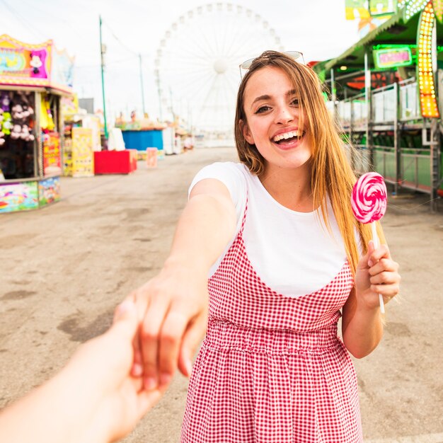 Primer plano de una persona que sostiene la mano de la mujer joven que sostiene la paleta en el parque de atracciones