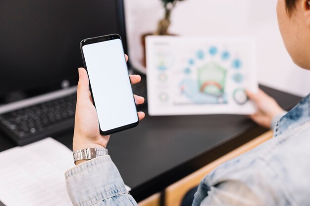 Primer plano de una persona que sostiene el teléfono móvil con pantalla en blanco en el lugar de trabajo