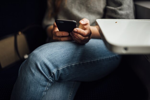 Primer plano de una persona sentada con las piernas cruzadas y sosteniendo un teléfono bajo las luces