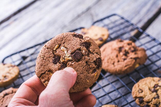 Primer plano de una persona sosteniendo una galleta con chispas de chocolate sobre un fondo borroso