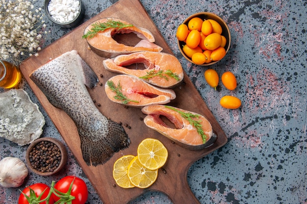 Primer plano de pescado crudo rodajas de limón verde pimienta sobre tabla de cortar de madera y flor en la tabla de colores negro azul