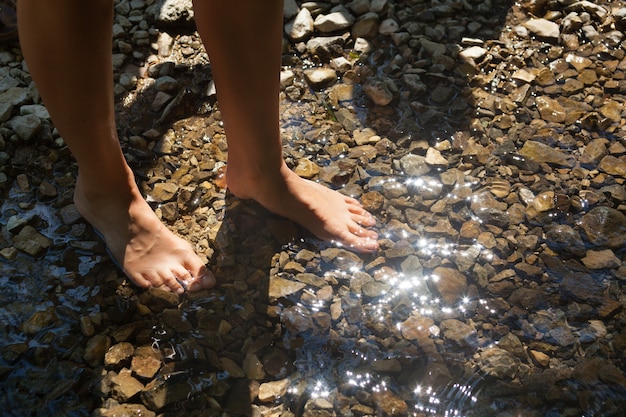 Primer plano del pie de un hombre en el agua del río lleno de pequeñas piedras