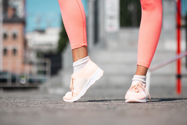 Primer plano de las piernas de la mujer vistiendo zapatillas deportivas rosa y leggings