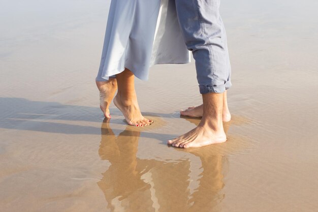 Primer plano de pies descalzos masculinos y femeninos sobre arena mojada. Hombre y mujer caminando en la playa con un borde de olas espumando suavemente debajo. Vacaciones, concepto de felicidad